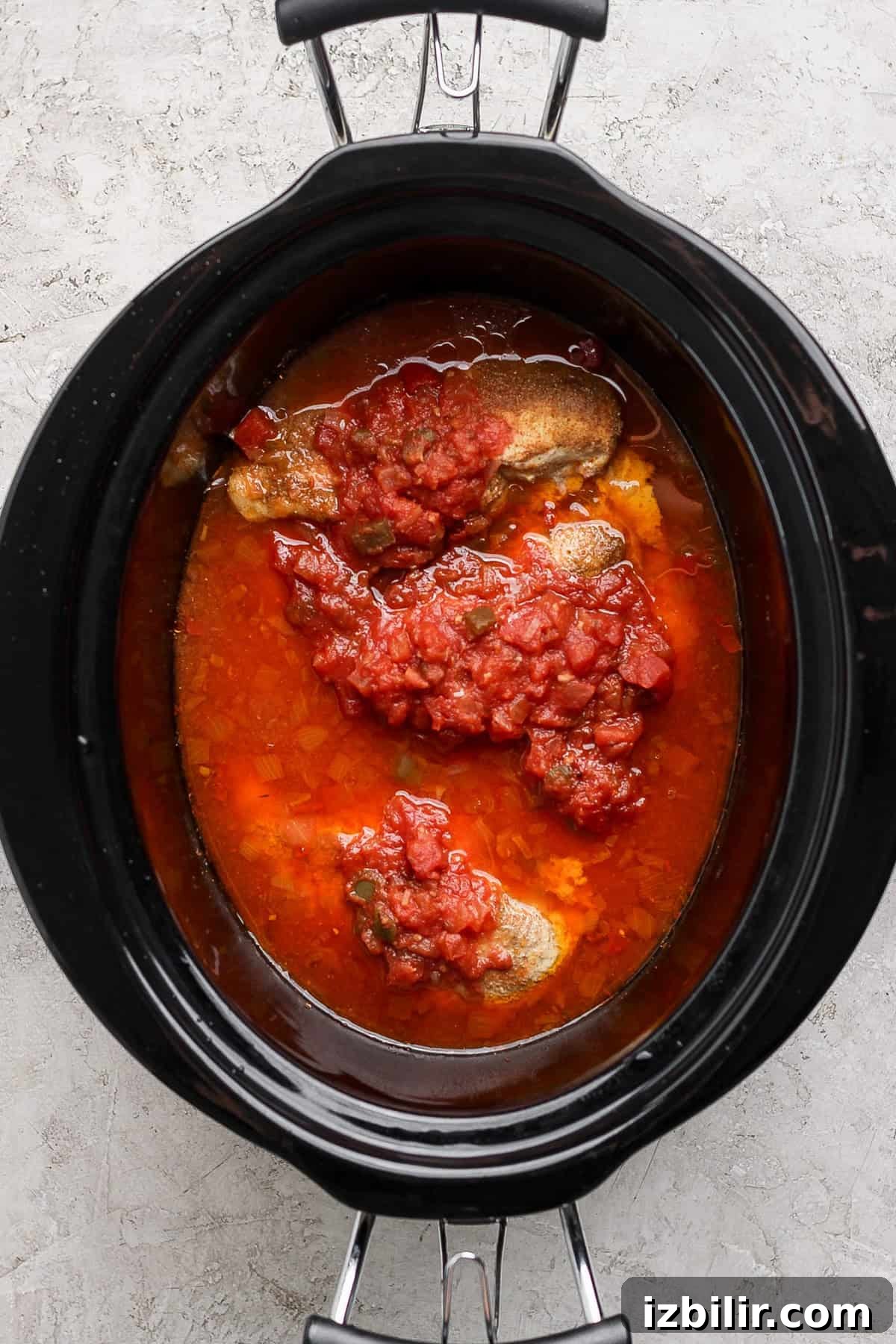 Slow cooker with beef and tomato sauce on a light surface.