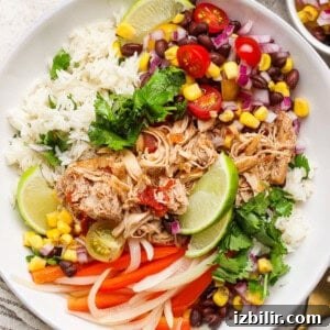 A bowl with shredded chicken, rice, black beans, corn, red onion, tomatoes, lime wedges, cilantro, and sliced bell peppers.