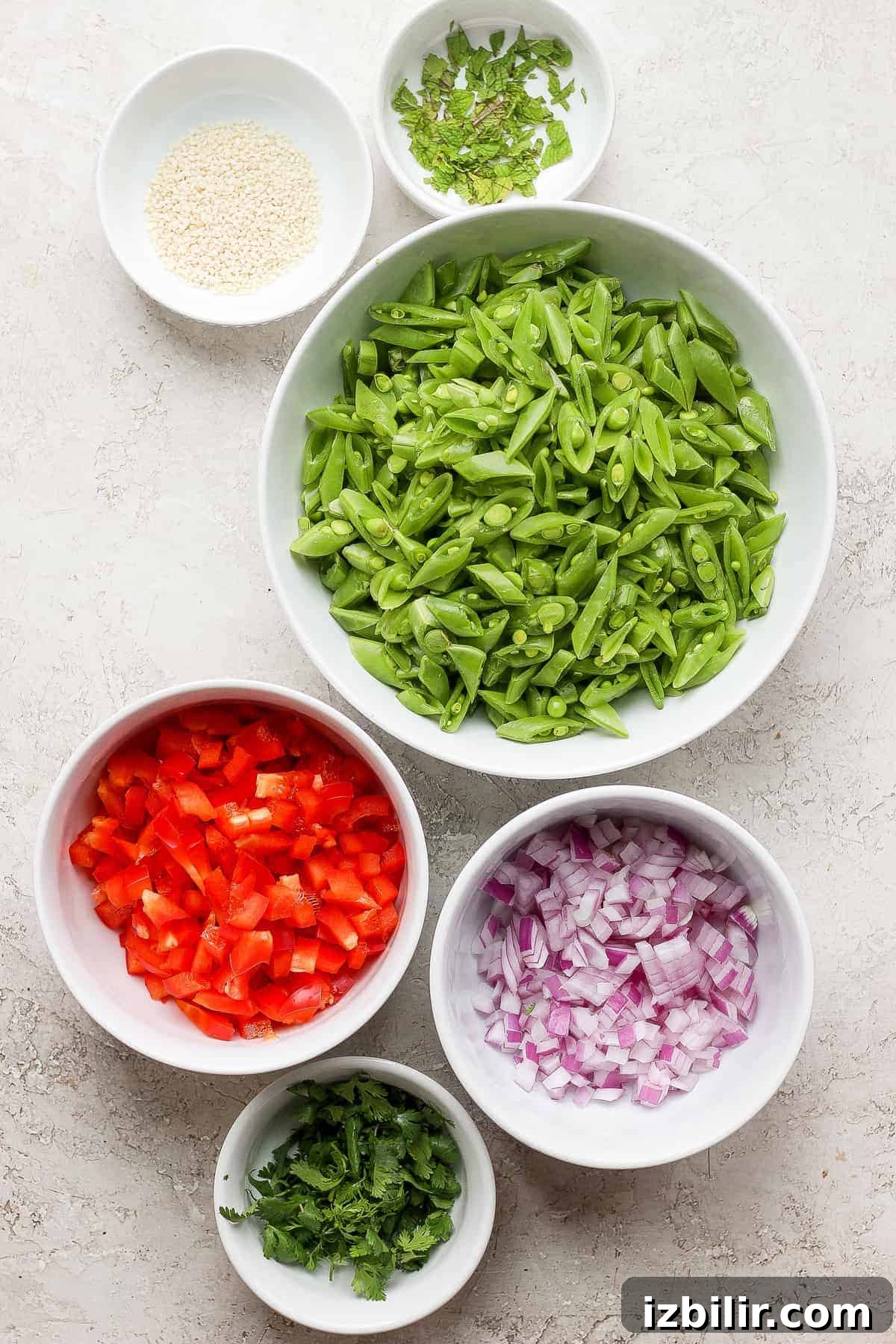 Sugar snap peas, red peppers, red onion, sesame seeds, and fresh mint in small bowls.