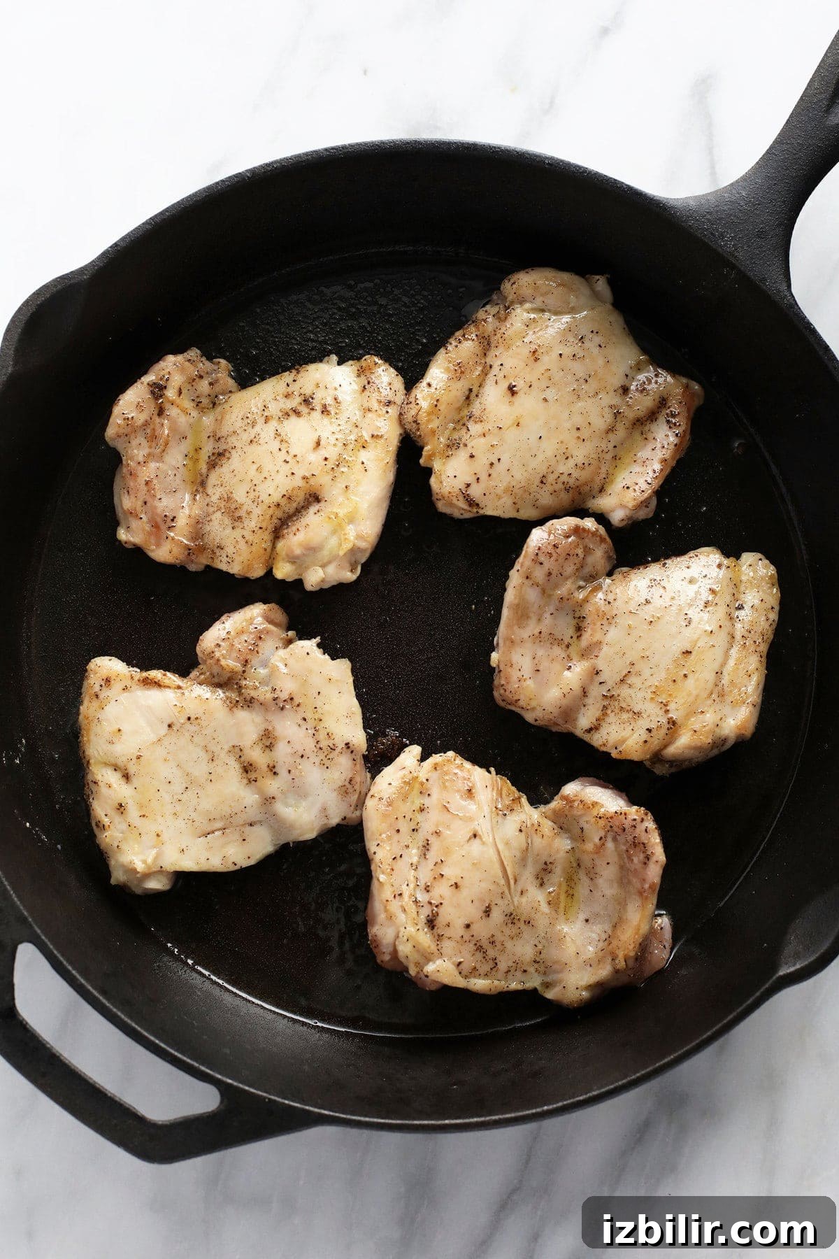 boneless skinless chicken thighs being seared in a cast iron skillet