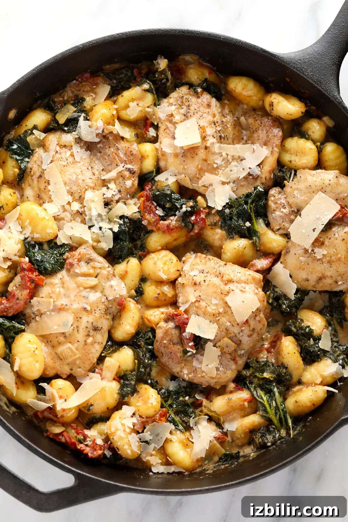 creamy tuscan chicken and gnocchi in a cast iron skillet topped with parmesan