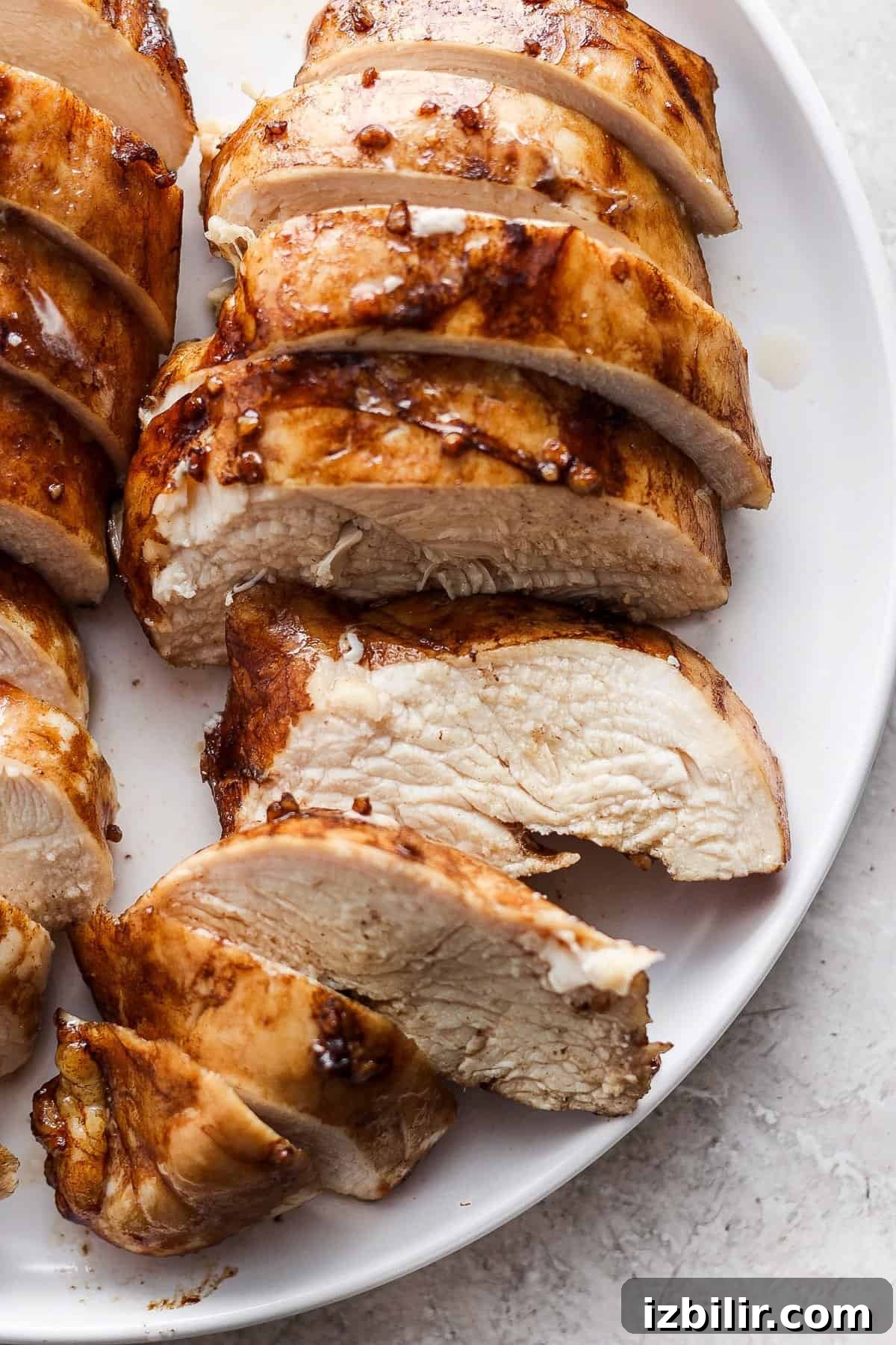 Sliced grilled chicken breast arranged on a white plate, showing juicy interior and golden-brown, seared exterior.