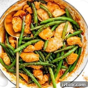 Kung Pao Chicken and green beans in a pan with sesame seeds.