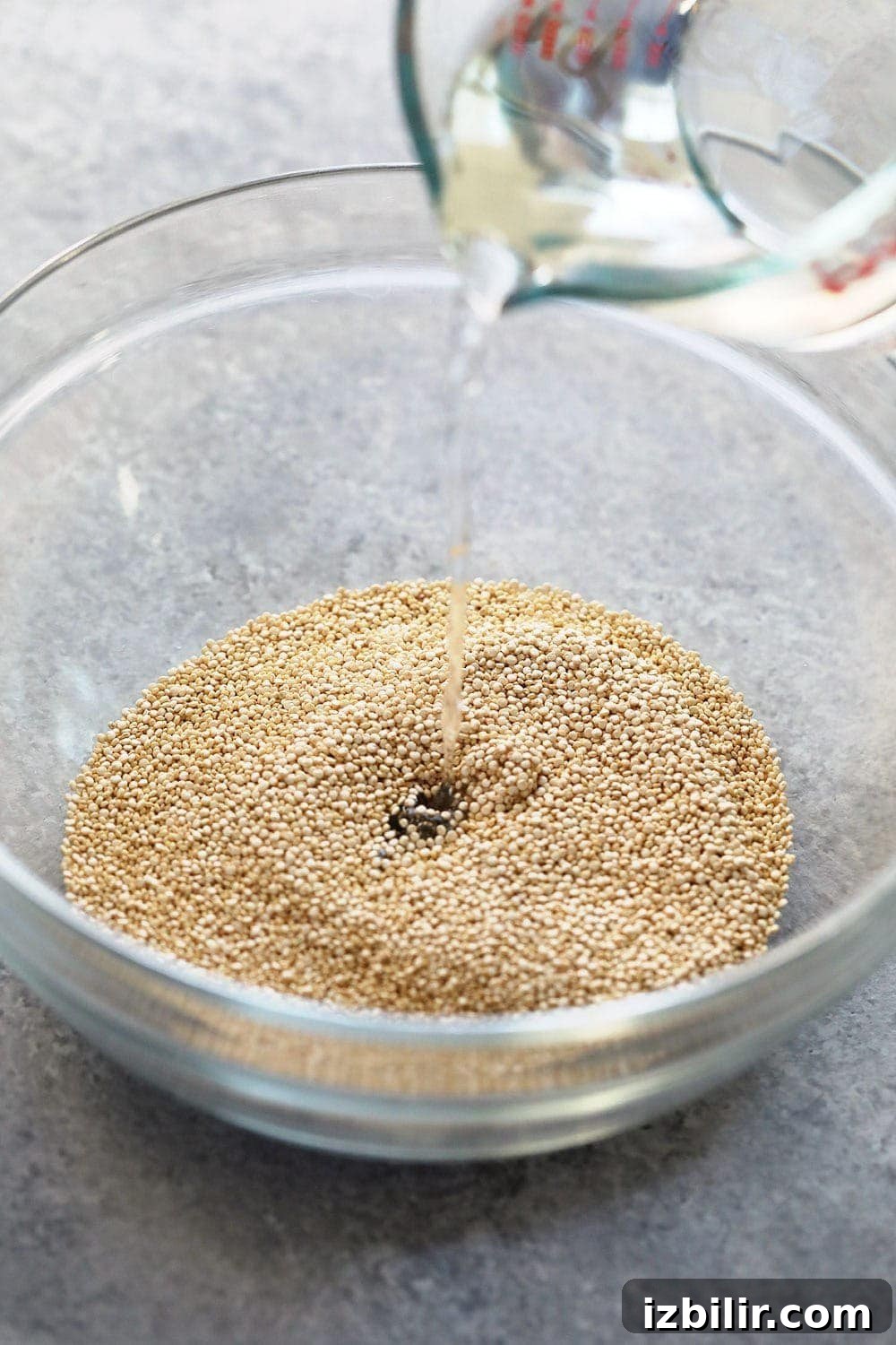 uncooked quinoa in a bowl with water being poured over it