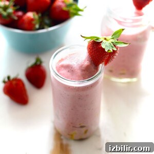 strawberry smoothie with pineapple chunks with strawberry on rim of glass