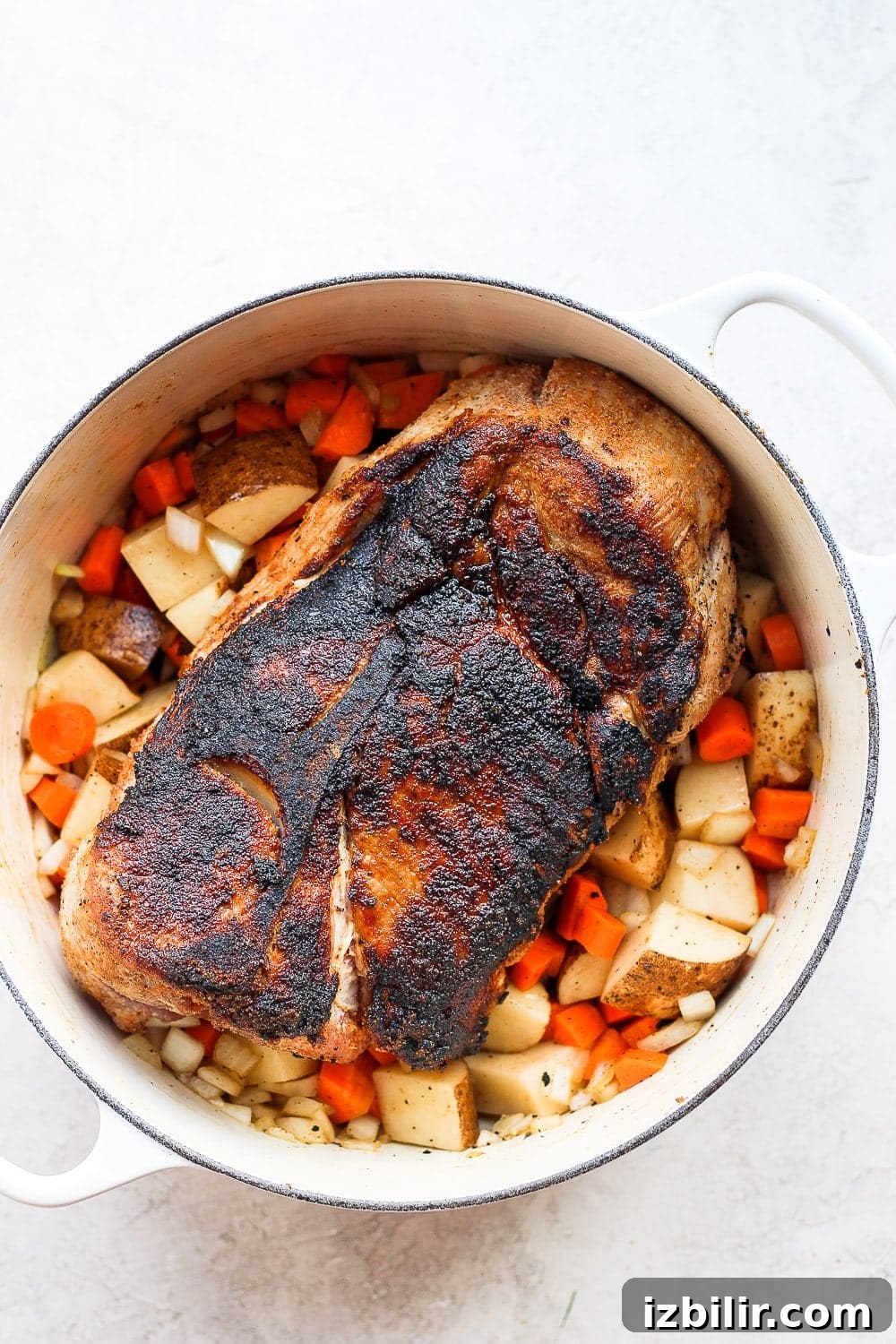 pork shoulder surrounded by veggies and ready to be roasted
