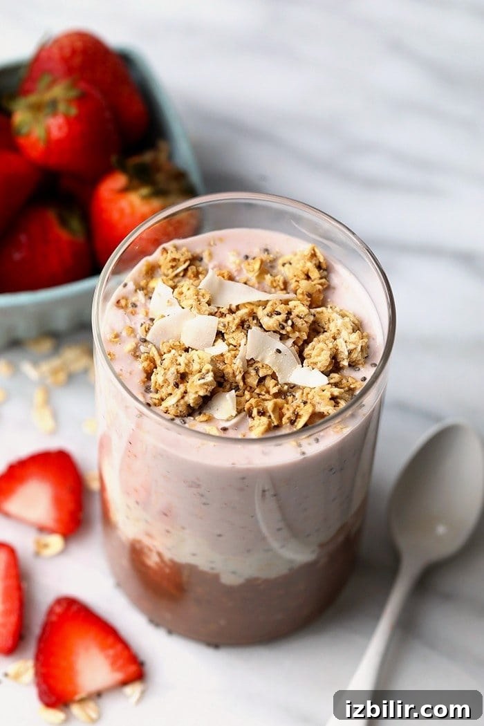 Neapolitan Overnight Oats: Chocolate, Vanilla & Strawberry 3 Overhead photo of Neapolitan overnight oats served in a glass jar with strawberries in the background.