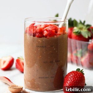A glass of overnight oats topped with strawberries and a spoon.