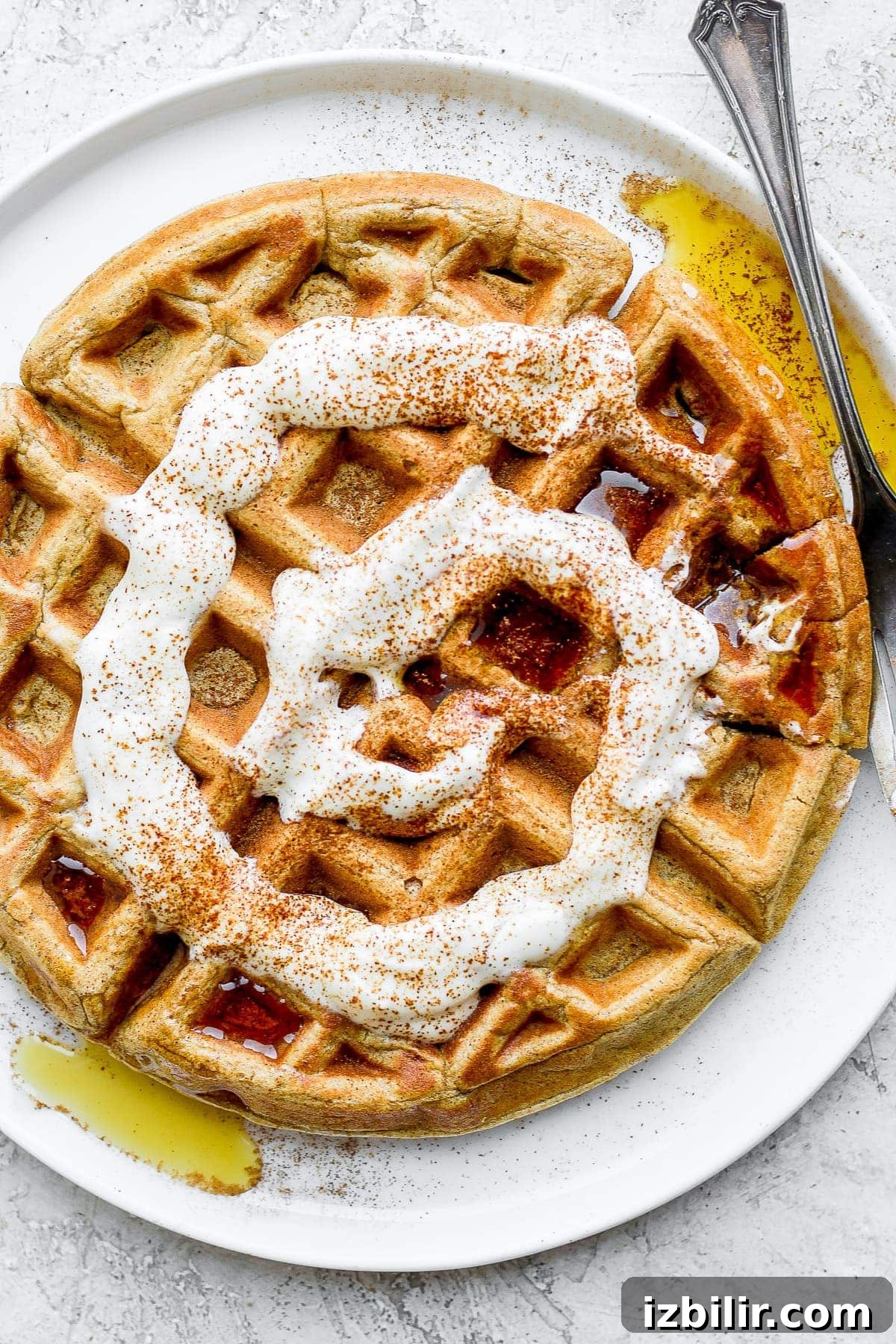cinnamon roll waffle on a plate with maple syrup and a cream cheese drizzle
