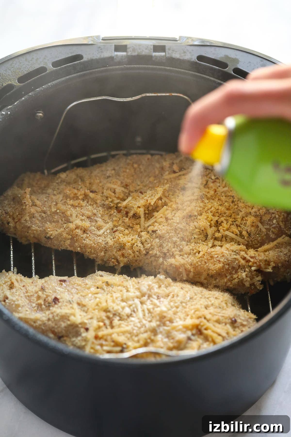 spraying chicken parmesan with cooking spray