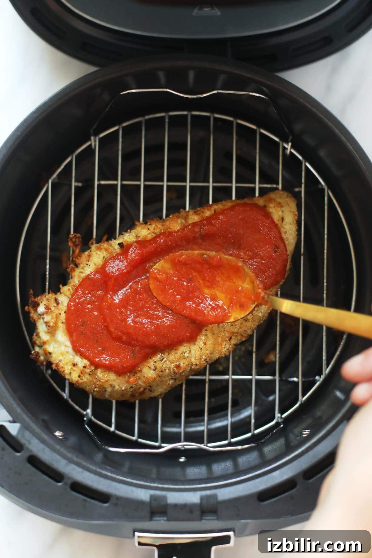 rubbing chicken parmesan with marinara sauce in air fryer
