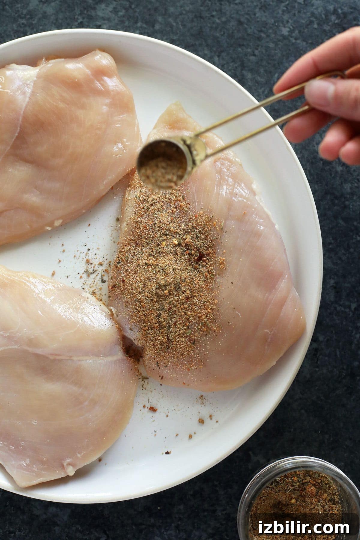 Sprinkling all purpose seasoning on a chicken breast.