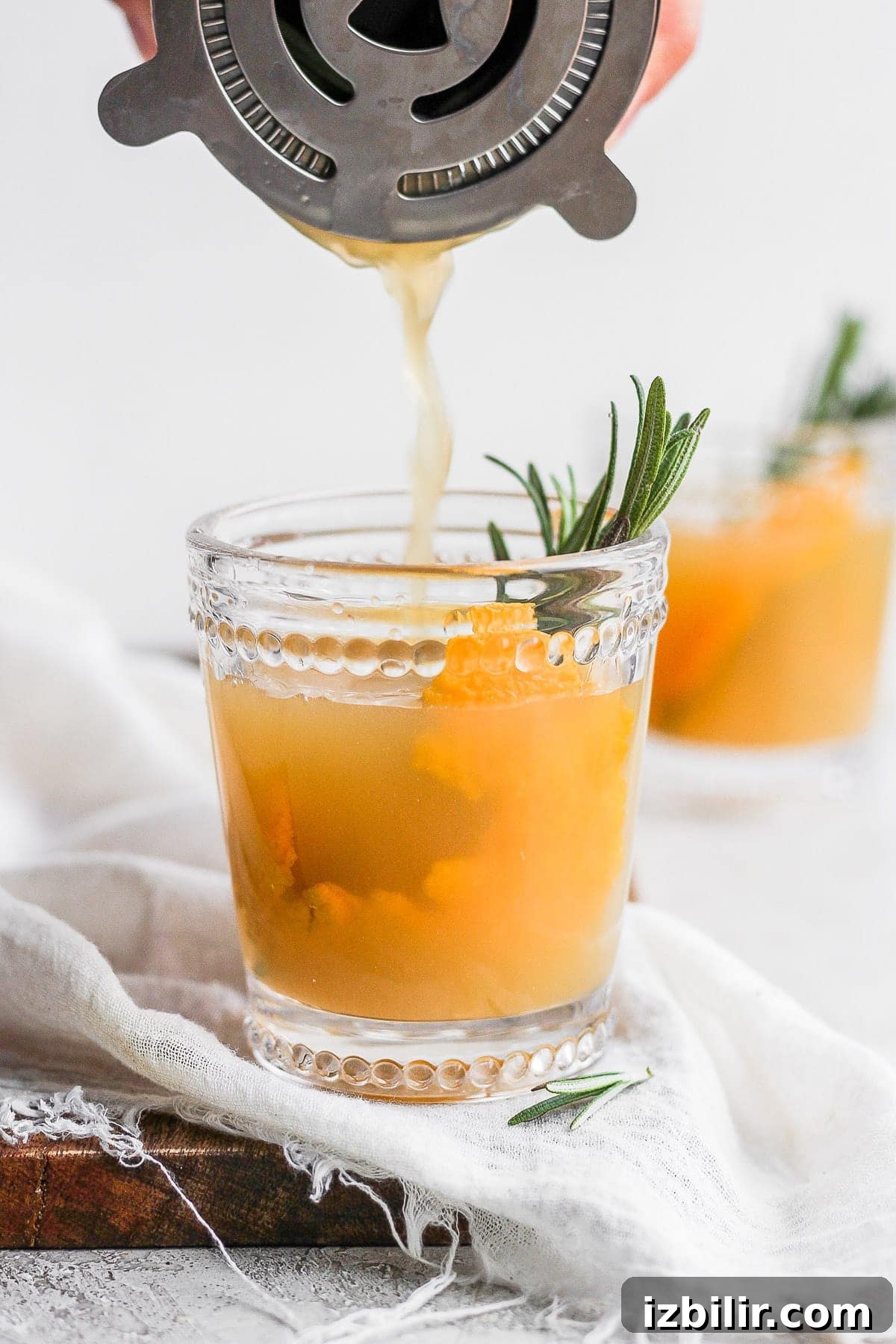 A festive Apple Cider Cocktail garnished with rosemary and orange peel