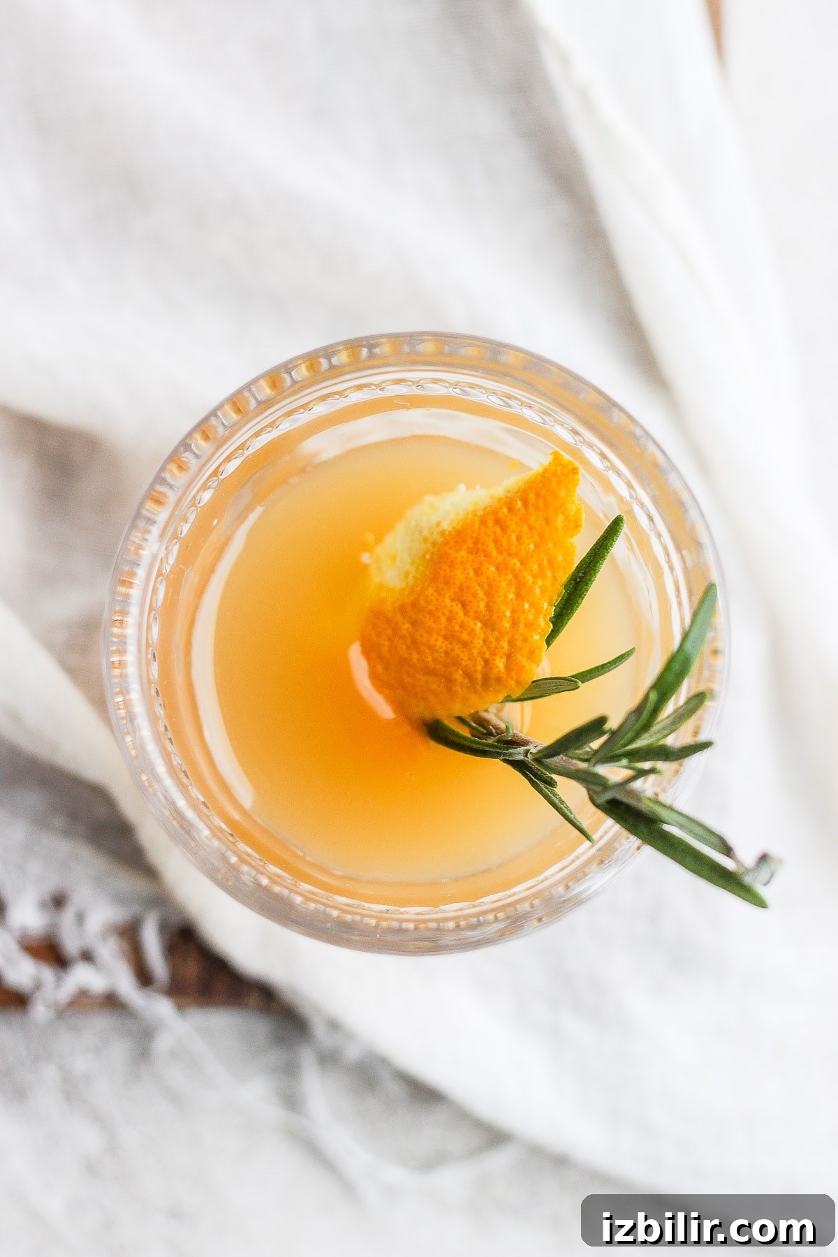 A punch bowl or pitcher of apple cider cocktail garnished with rosemary