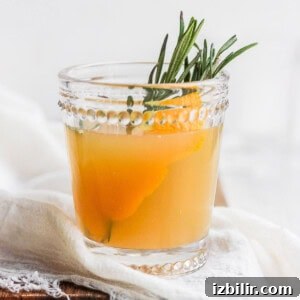 A glass of apple cider cocktail with rosemary sprigs