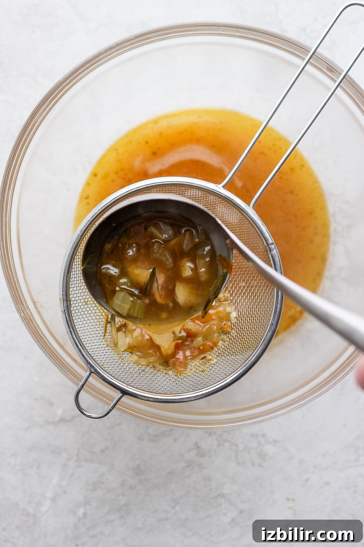 Pouring chicken broth through a sieve.