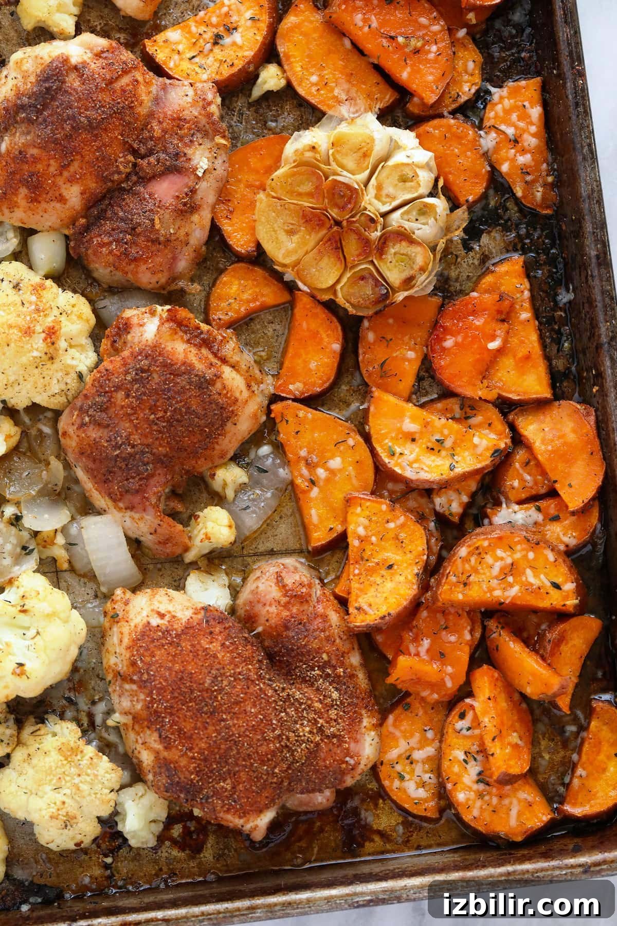 Chicken, sweet potatoes, cauliflower, onion, and garlic on a baking sheet.