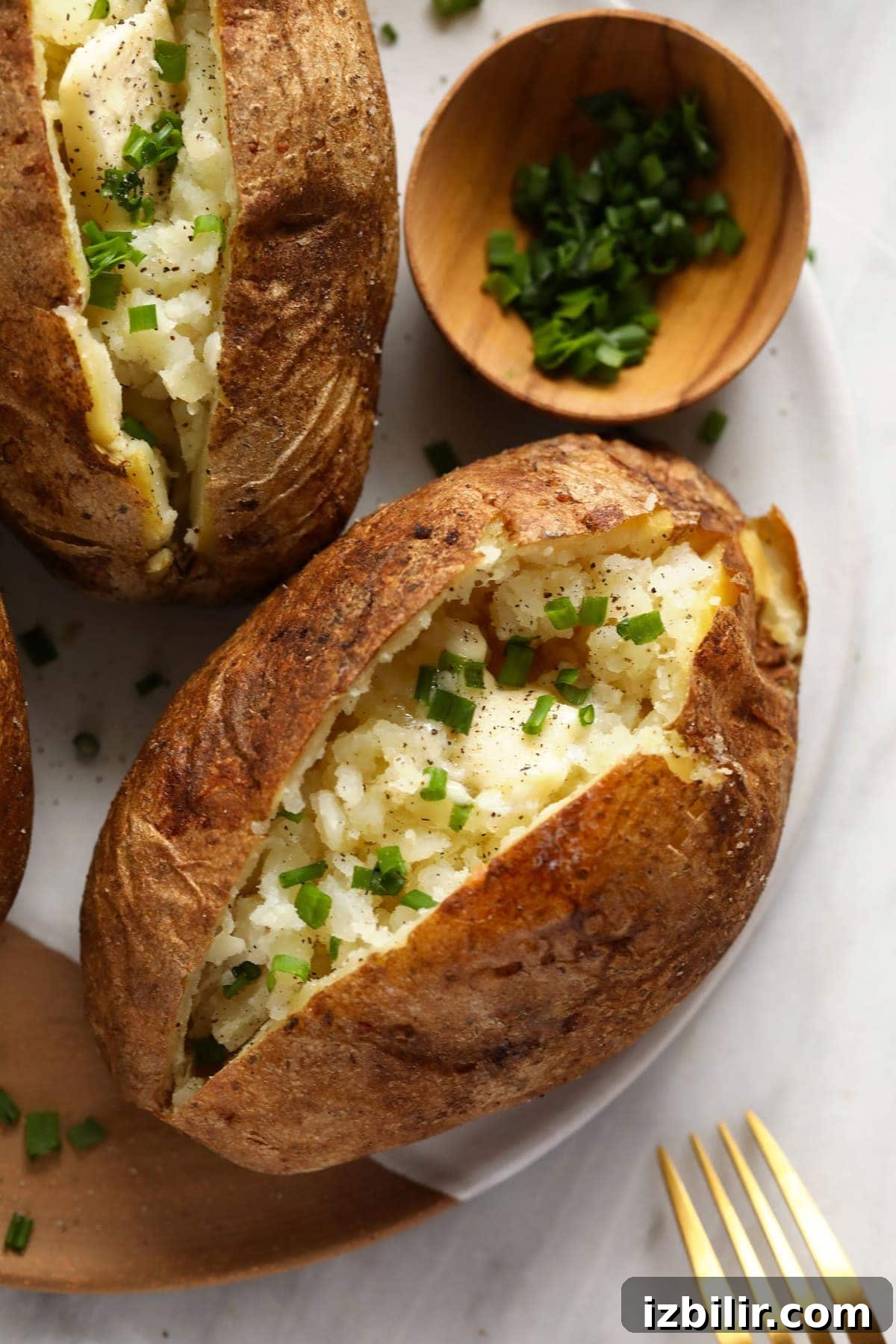 Baked potatoes on a plate with butter, salt, pepper, and chives.
