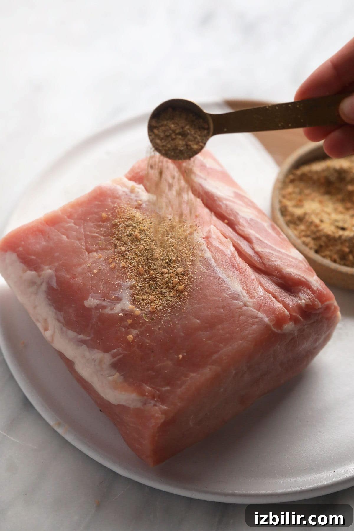 Raw pork loin roast being seasoned.