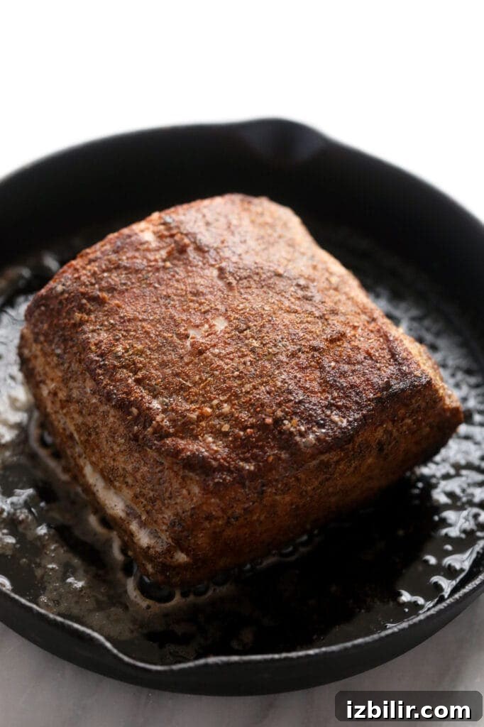 Slow cooker pork loin being seared in a cast iron skillet.
