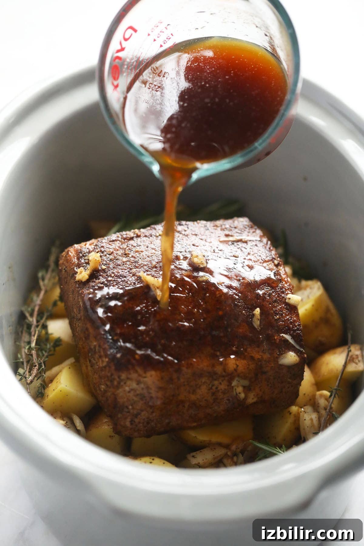 Pork loin roast on a bed of potatoes being placed in a slow cooker.