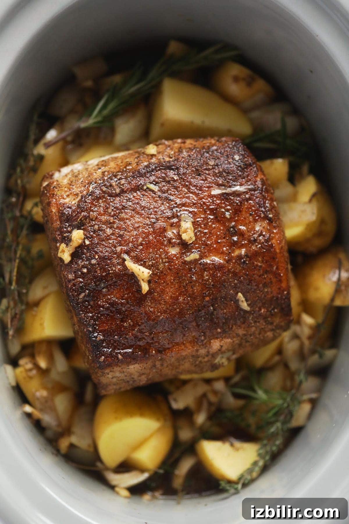 Slow cooker pork loin roast on a bed of potatoes and herbs.