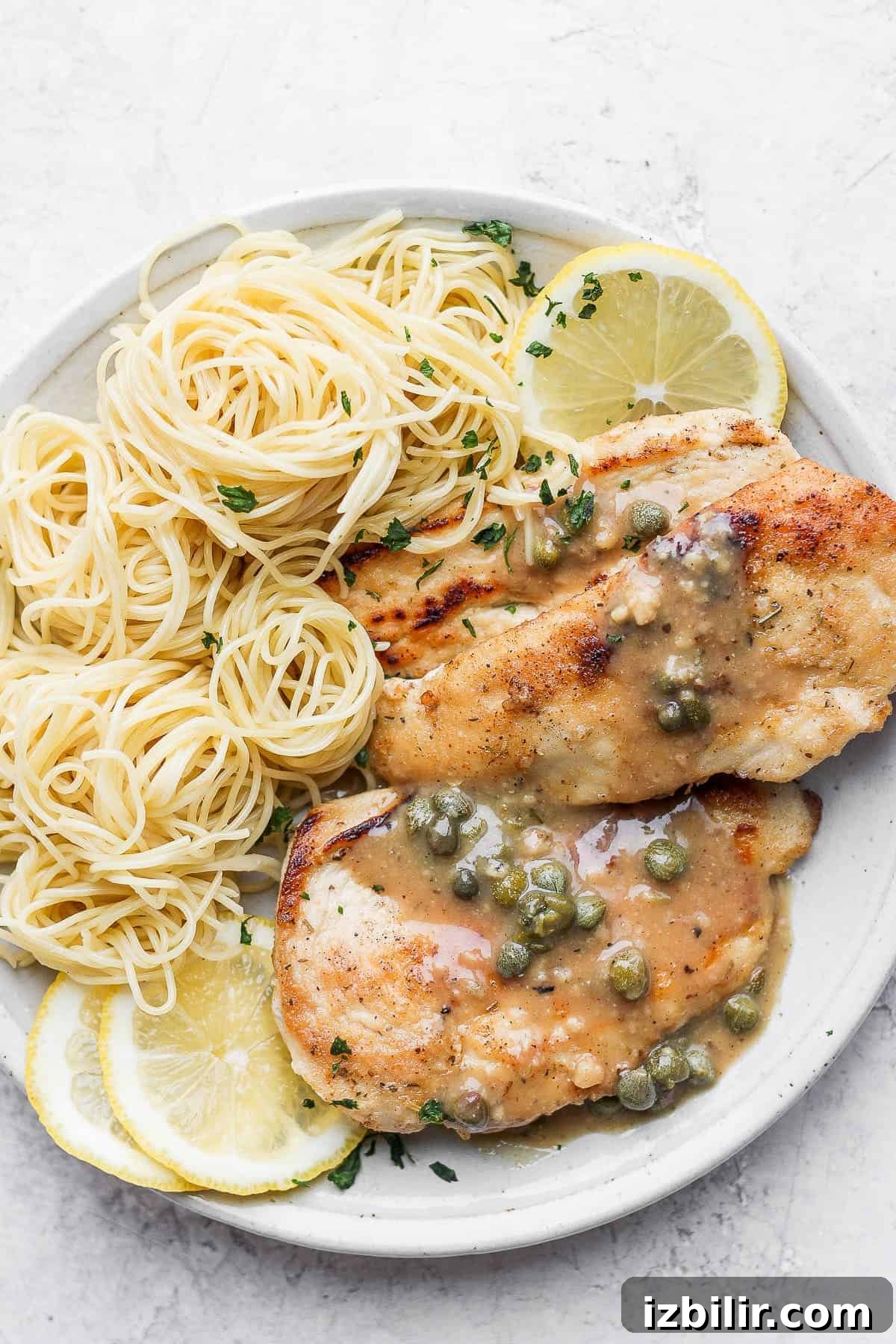 Chicken piccata on a plate with angel hair pasta.