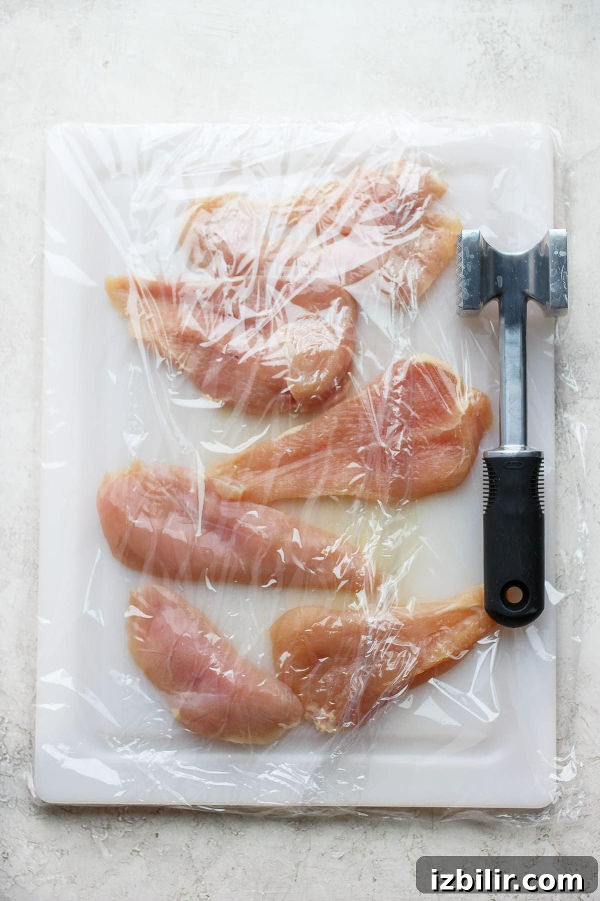 Pounding chicken breast on a cutting board with a meat cleaver.