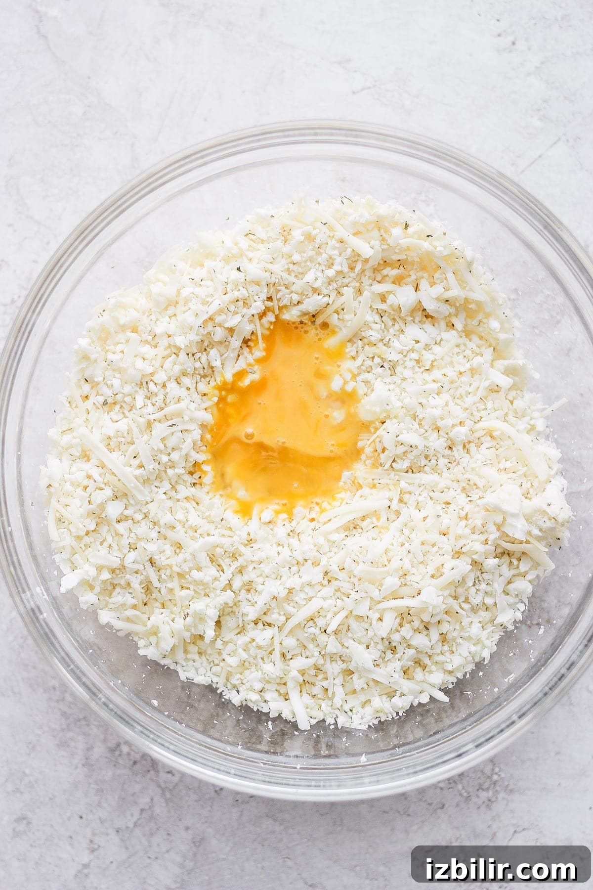 Gluten-Free Cauliflower Pizza Crust Recipe 5 Cauliflower rice in a bowl with cheese and a whisked egg.