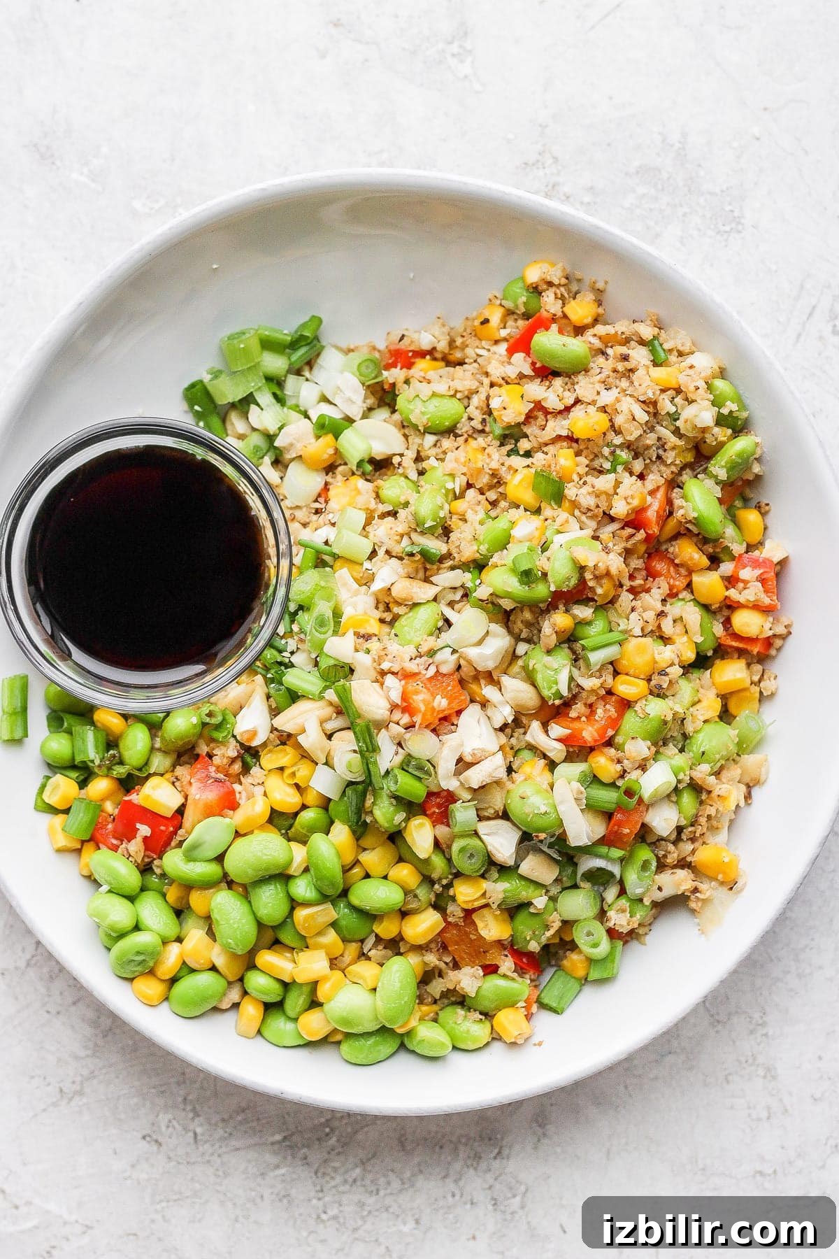 This Cauliflower Fried Rice recipe is a delicious low carb alternative to traditional fried rice. Packed with veggies and a super flavorful sauce, plus it's easy to make. Enjoy! cauliflower fried rice in a bowl next to the sauce