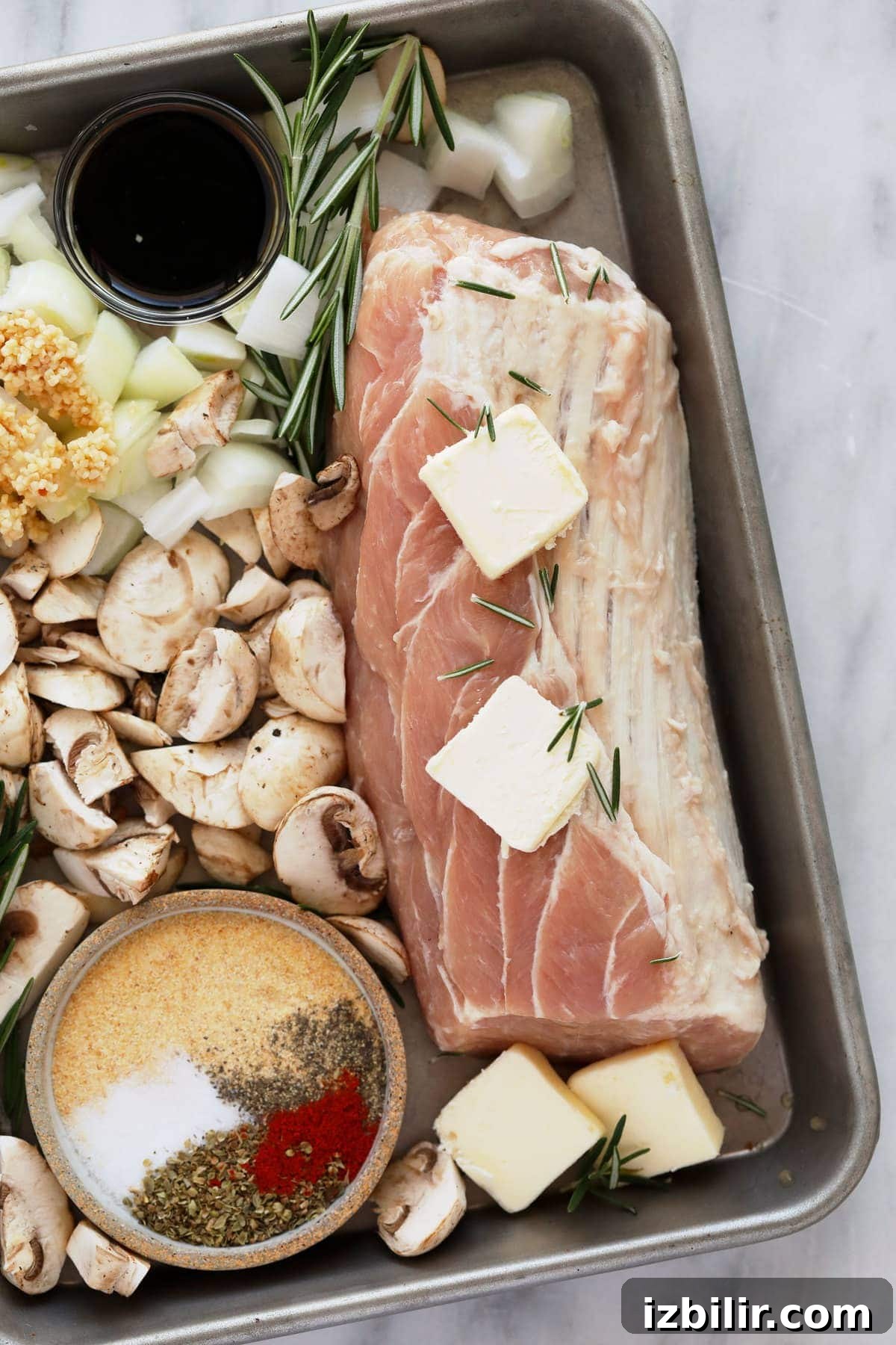 This is hands down the best pork tenderloin recipe — tender and juicy with a gravy that's to die for. raw pork with mushrooms and butter on sheet pan.
