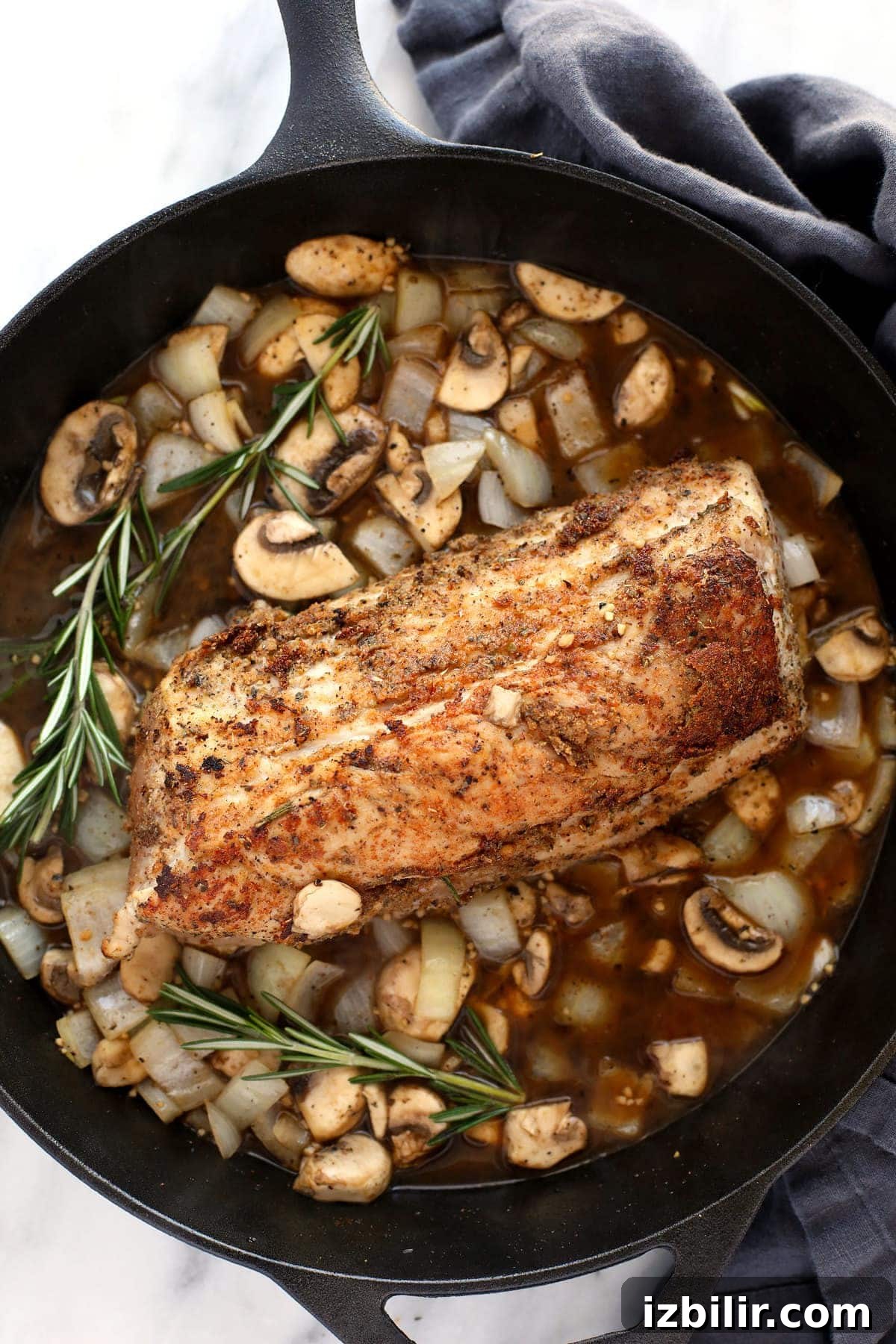 Baked pork tenderloin topped with mushroom gravy pork tenderloin in gravy on cast iron pan.