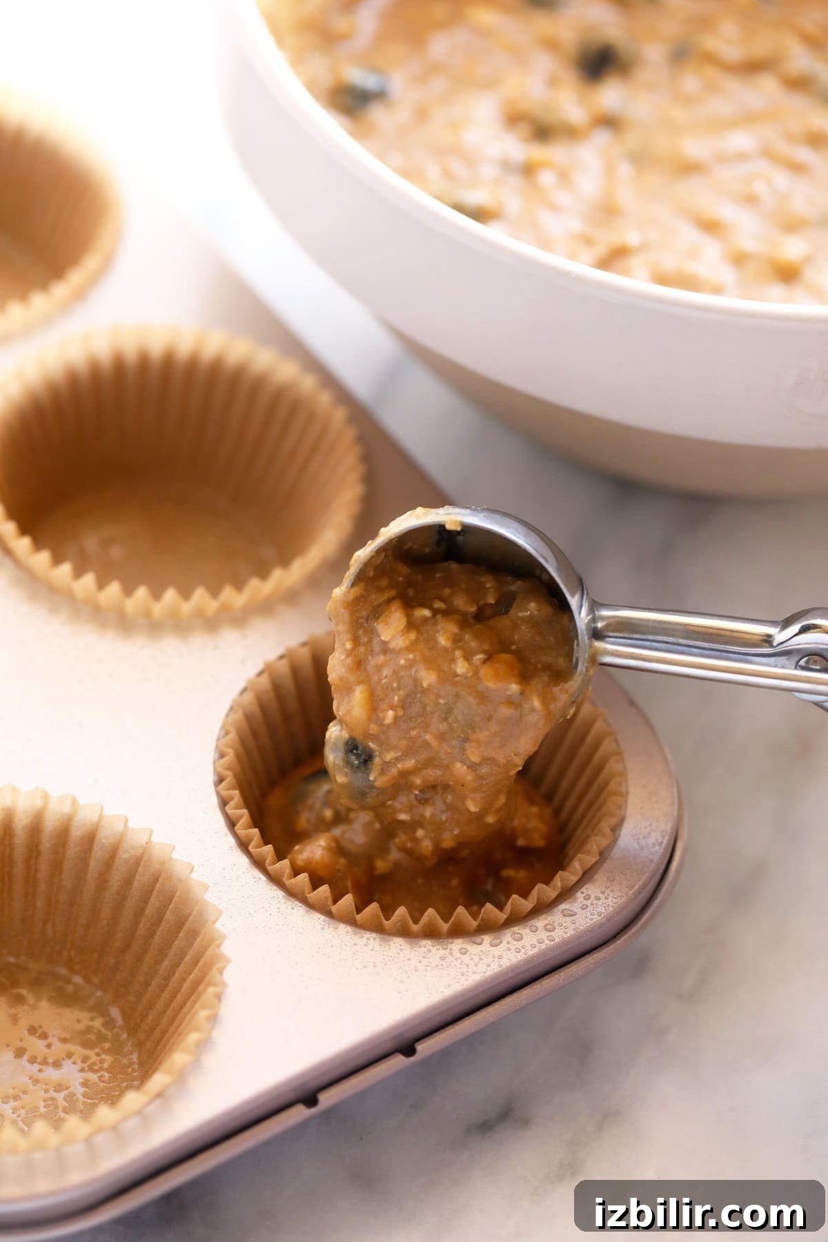 blueberry muffin batter being poured into muffin liners