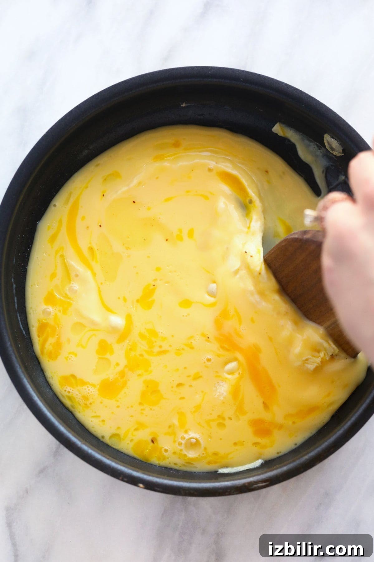 Scrambled eggs being folded in a nonstick pan scrambled eggs in a non stick pan being cooked over medium heat and stirred with a wooden spatula