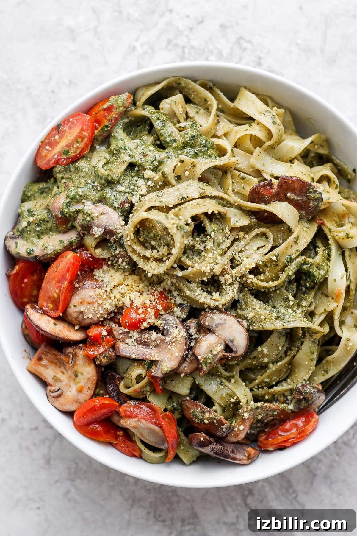Vegan pesto pasta with tomatoes, mushrooms, pesto, and vegan parmesan.