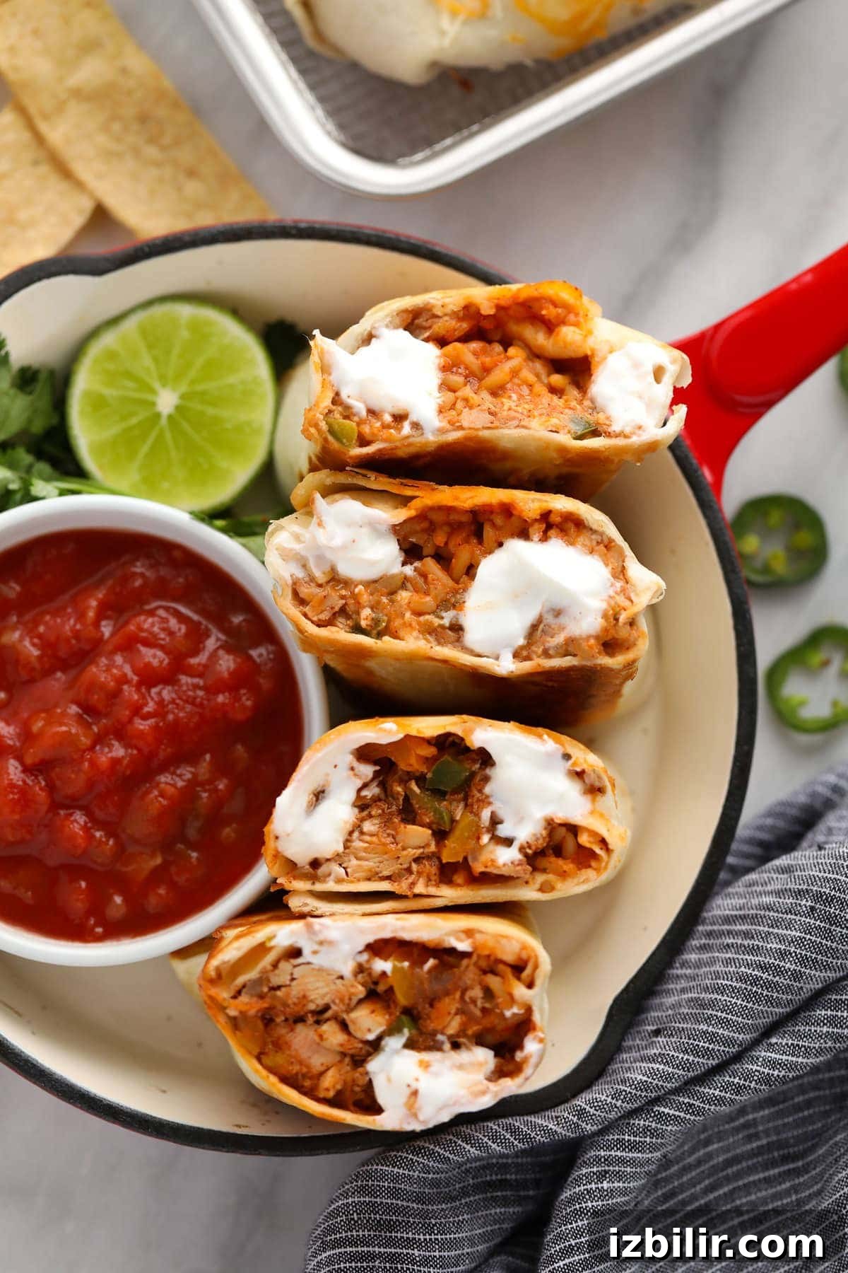 Shredded chicken burritos cut in half with a bowl of salsa.