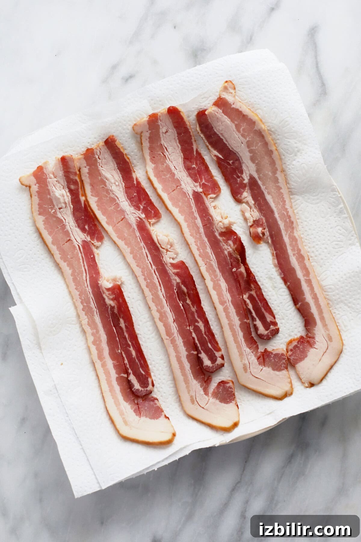 Crispy Microwave Bacon in Minutes 3 Raw bacon on a plate on top of paper towel.