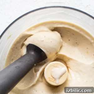 A blender filled with creamy banana nice cream, with a black tamper blending the mixture.
