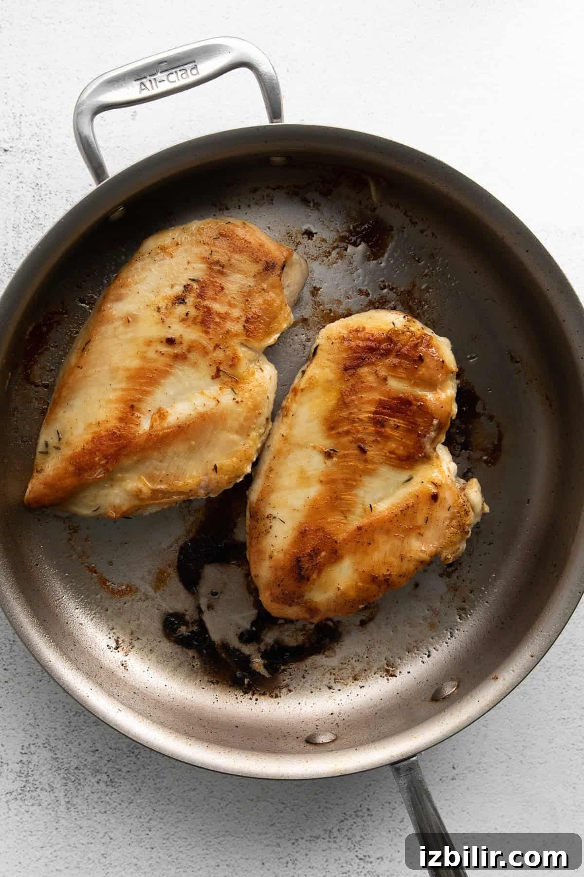 Homemade Creamy Chicken Alfredo 4 Two cooked chicken breasts in a stainless steel skillet. The chicken has a golden-brown sear and the pan shows some residual cooking marks.