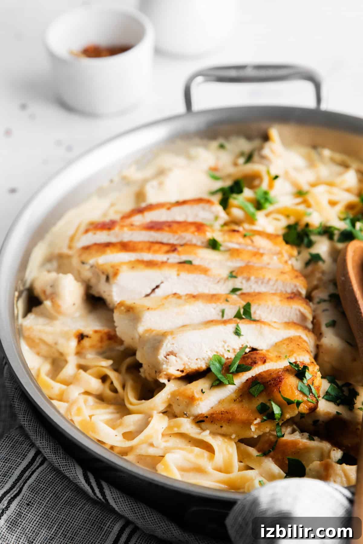 Homemade Creamy Chicken Alfredo 5 A skillet containing creamy fettuccine Alfredo topped with sliced grilled chicken and garnished with chopped parsley.