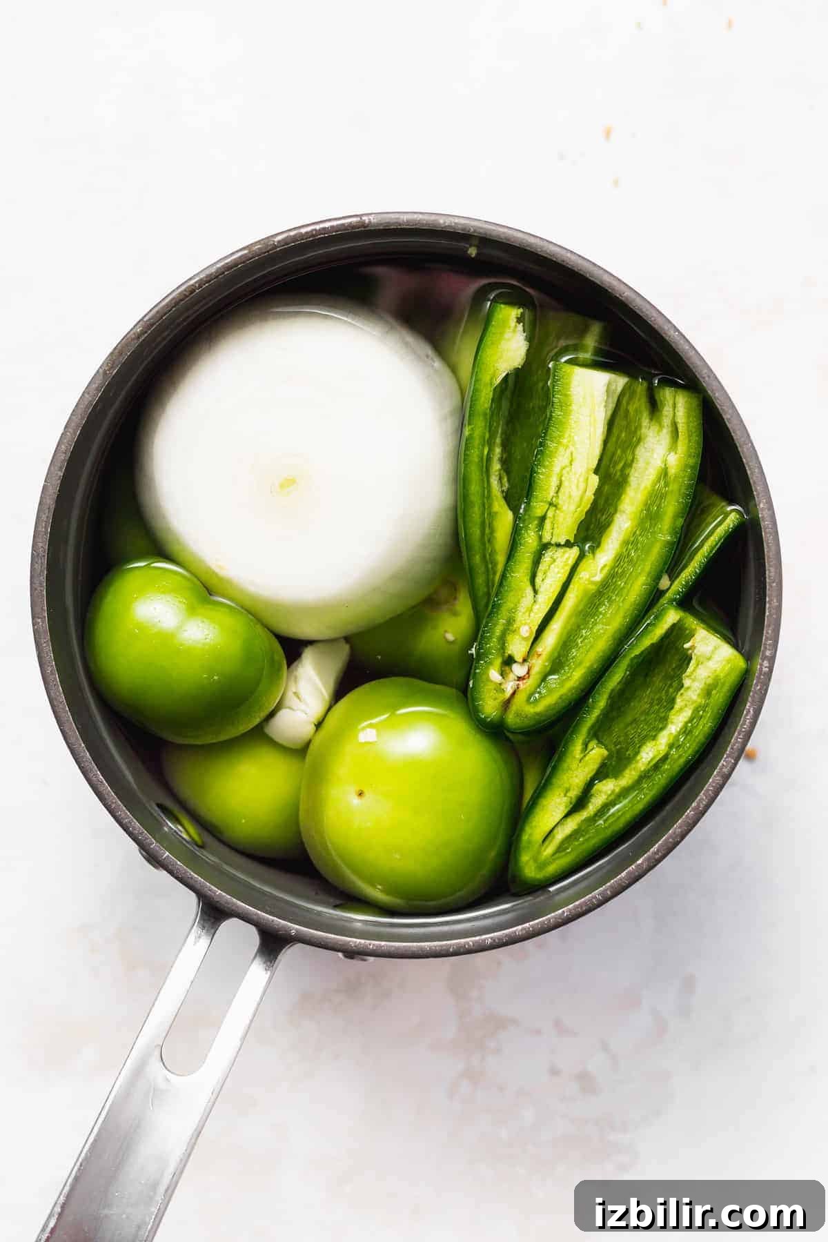 Tomatillos, garlic, onion, jalpeños, and other ingredients in a saucepan.