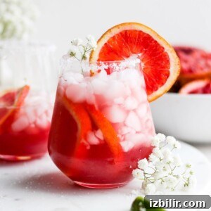 two glasses of grapefruit margarita adorned with ice and flowers