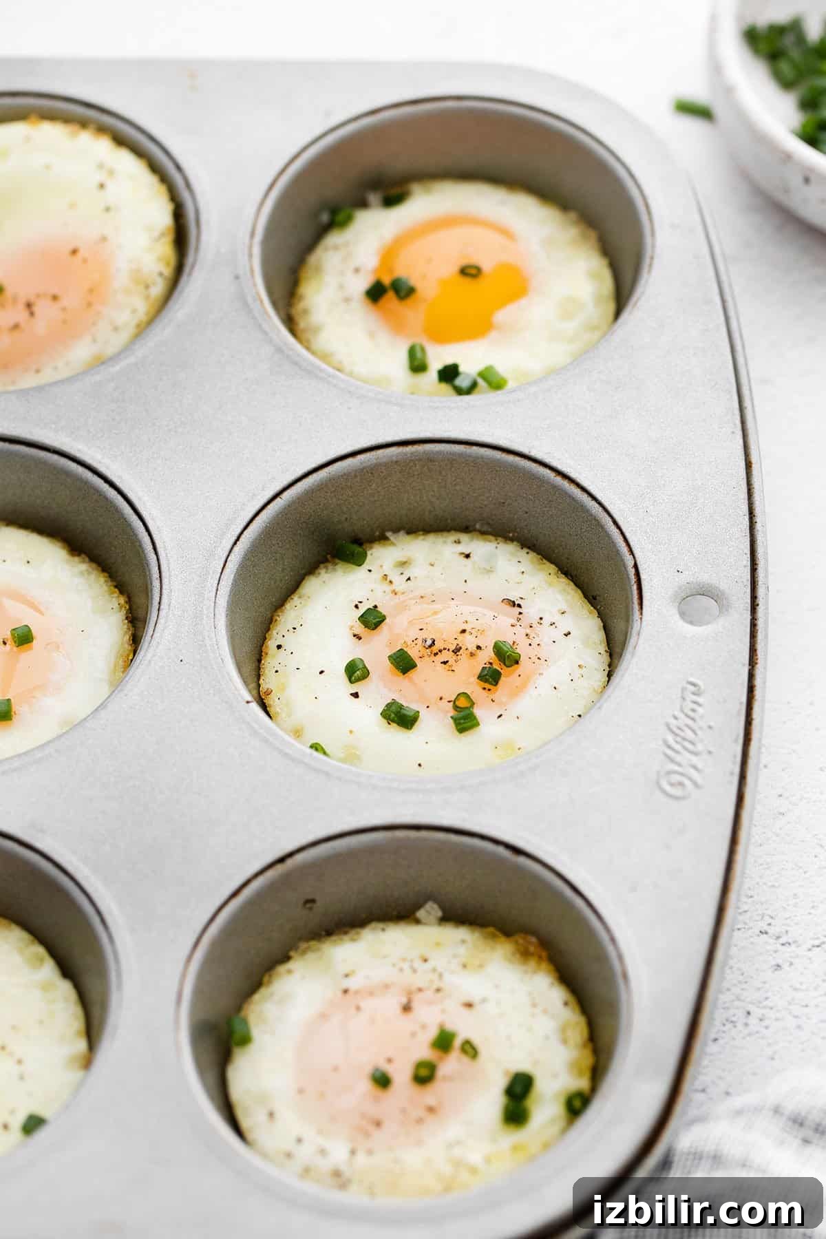 Instructions for baking eggs in the oven using a muffin tin, topped with fresh chives.