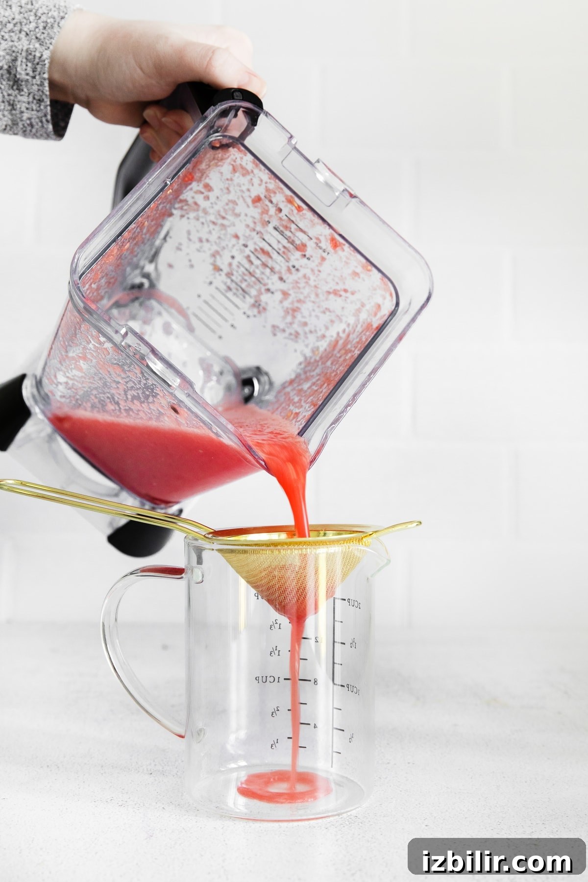 Pouring blended watermelon through a sieve.