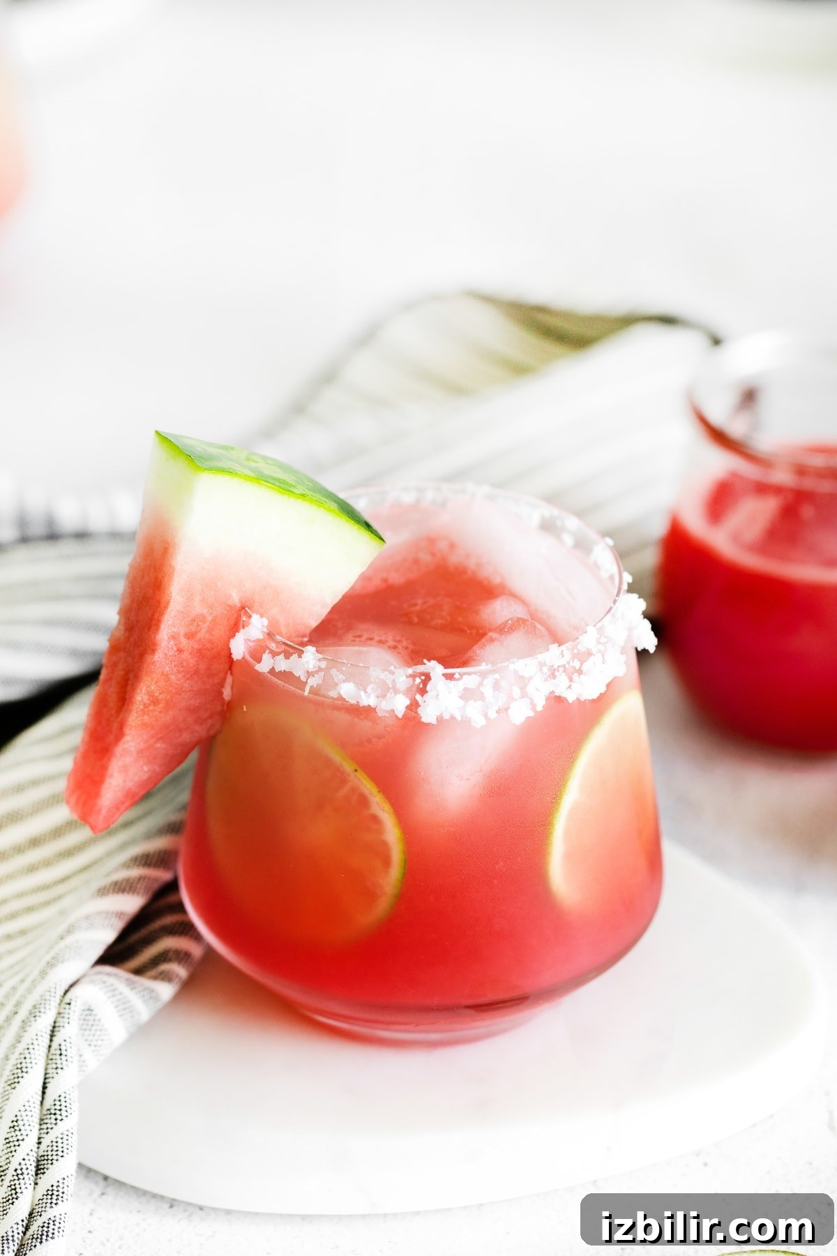 Watermelon margarita in a glass with a salted rim, lime rounds, and fresh watermelon.