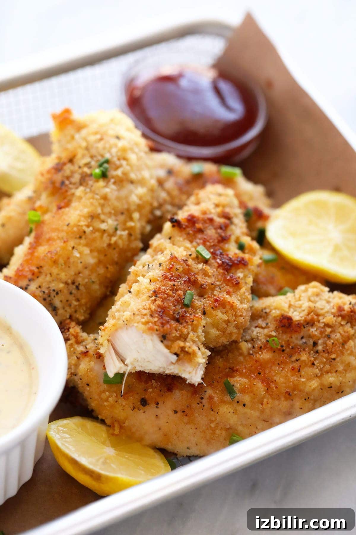 Chicken tenders in a basket with ketchup, lemons, and honey mustard.