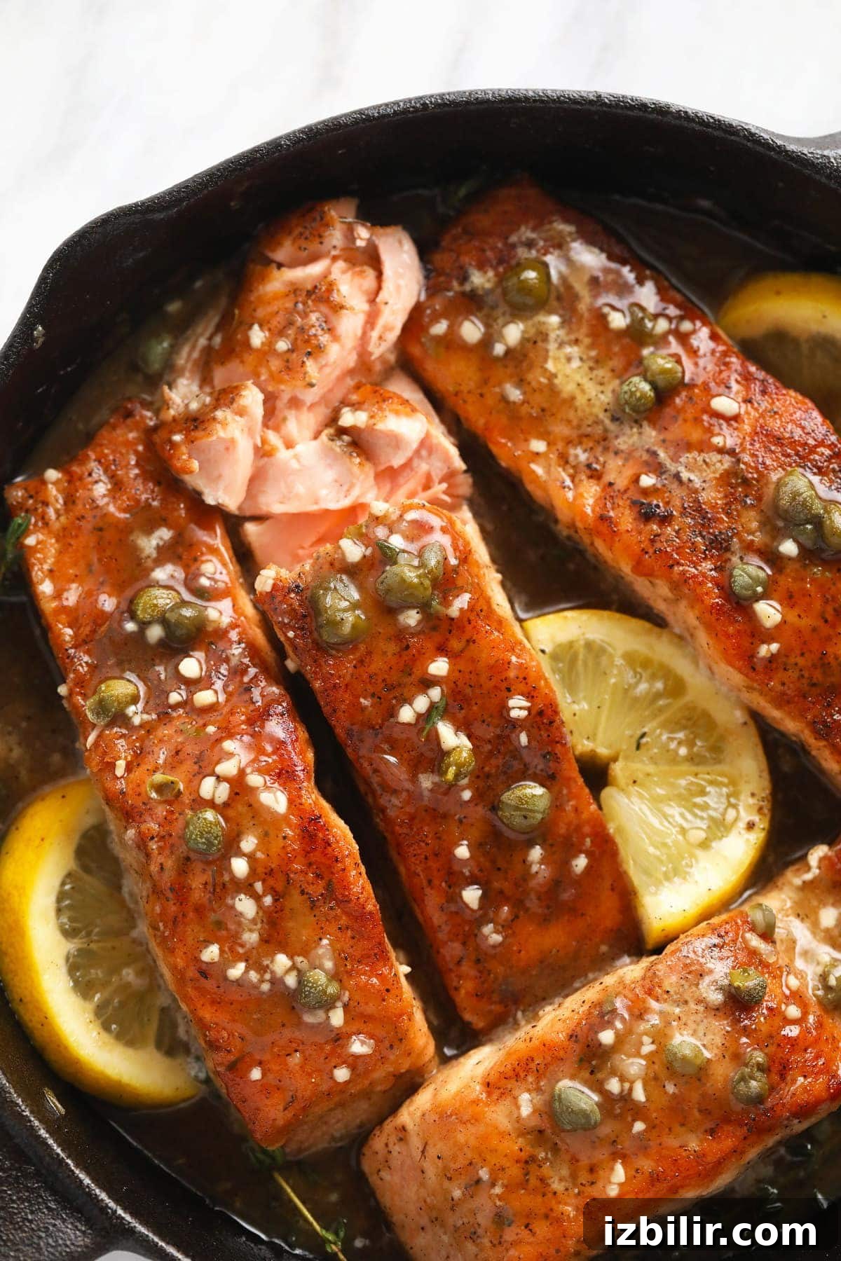 Pan-Seared Salmon Piccata with Lemon Caper Sauce 7 Salmon piccata in a cast iron pan with lemons, capers, and garlic.