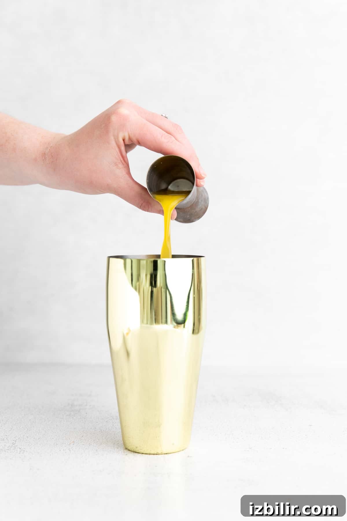 pouring orange juice into a cocktail shaker.
