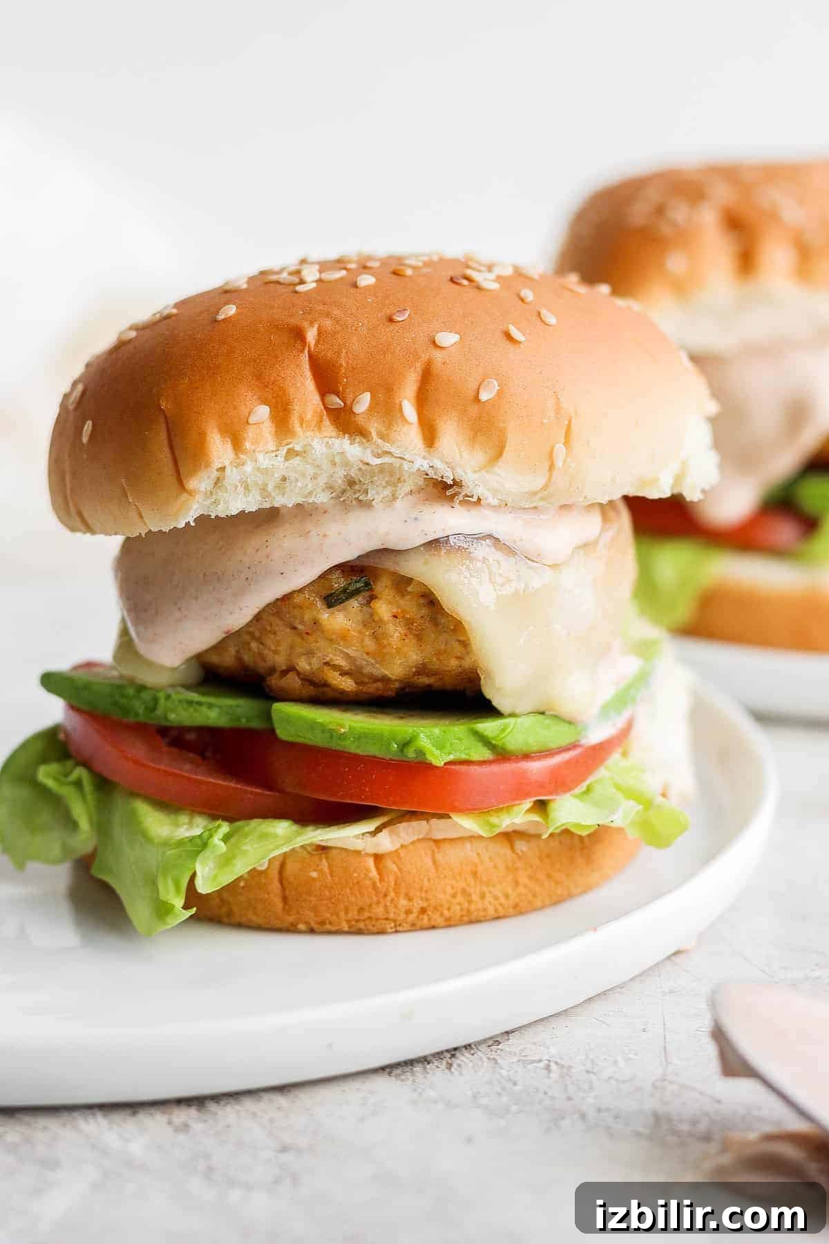 chicken burger on bun with avocado and tomato.