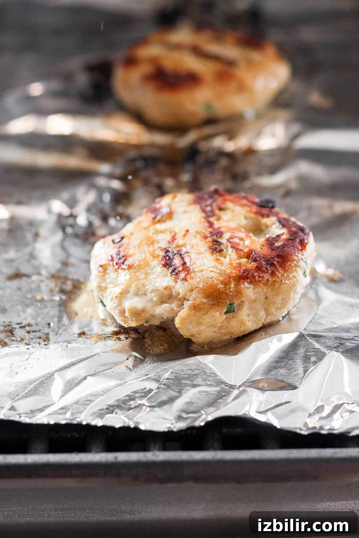 ground chicken burger on tin foil on grill.